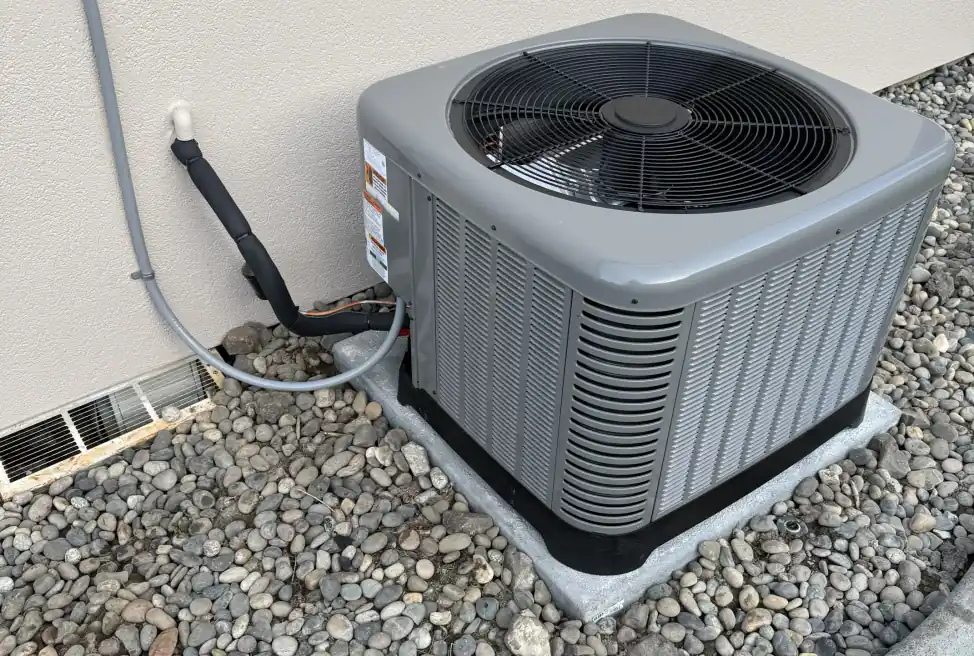 New grey condenser installed on a pad in river rock