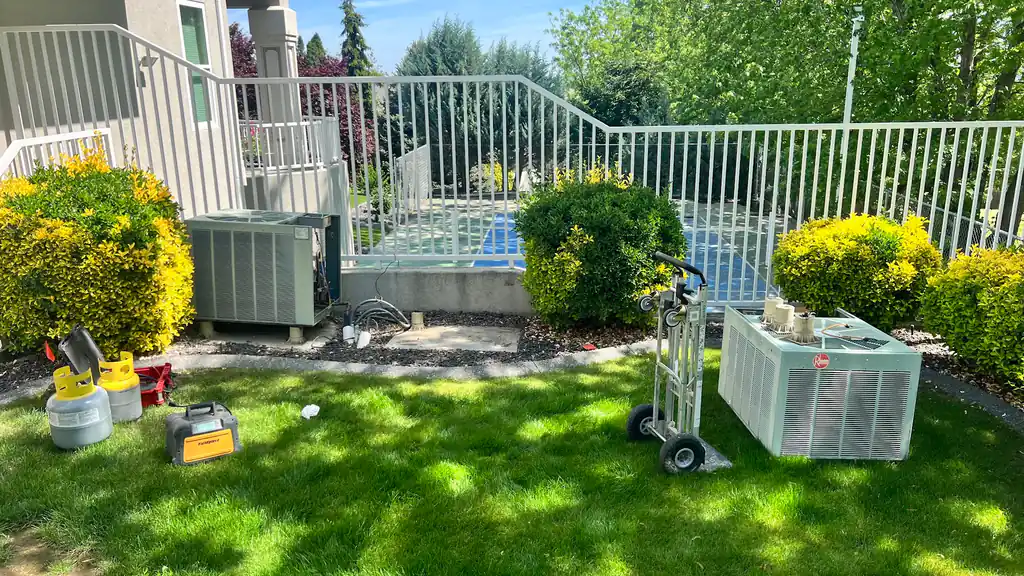 An old Rheem condenser on a hand truck beside a pool fence, recovery tanks on the lawn