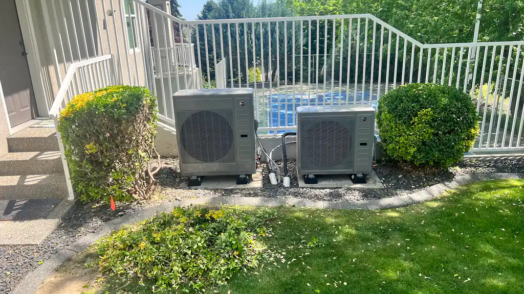 Two new heat pump outdoor units set on pads beside a pool fence